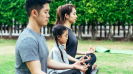 Happy Asian family is spending their holidays enjoying yoga in park together happily.