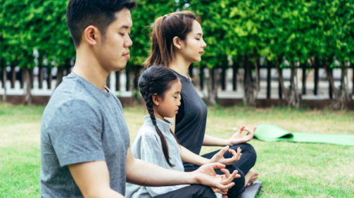 Happy Asian family is spending their holidays enjoying yoga in park together happily.